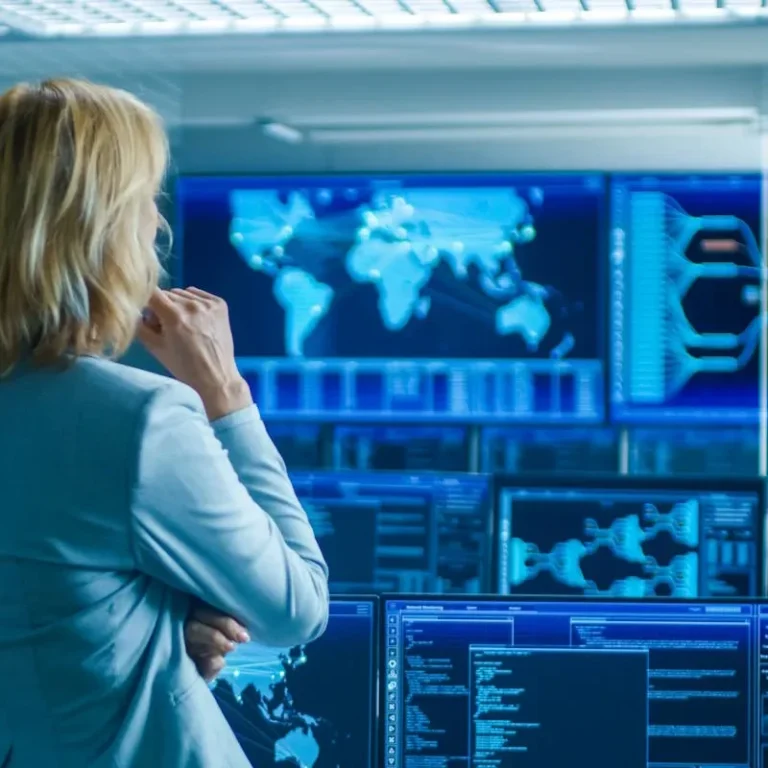 Frau vor Monitoren mit Weltkarte Operator monitoring global infrastructure networks on multiple screens in a modern control centre."